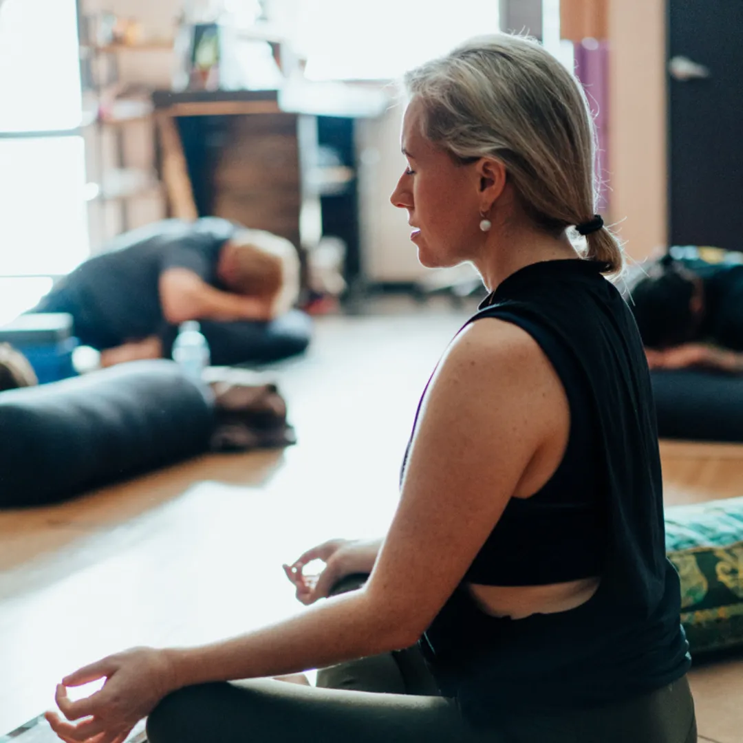 A young person sitting cross‑legged in a calm, softly lit space, eyes closed and hands resting on knees, practicing daily meditation for stress relief.