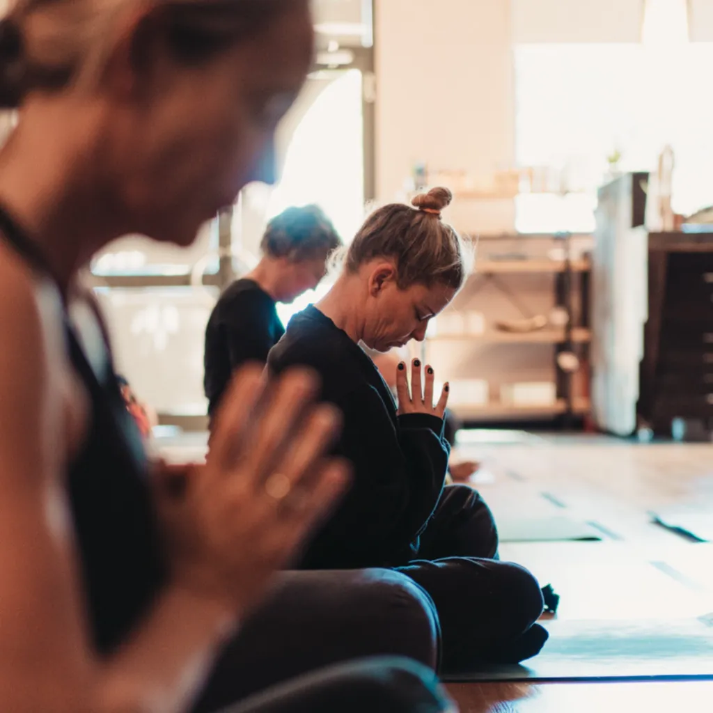 Person seated in a peaceful meditation pose on a yoga mat with hands resting on heart, eyes closed and steady breath, representing discipline and gratitude.