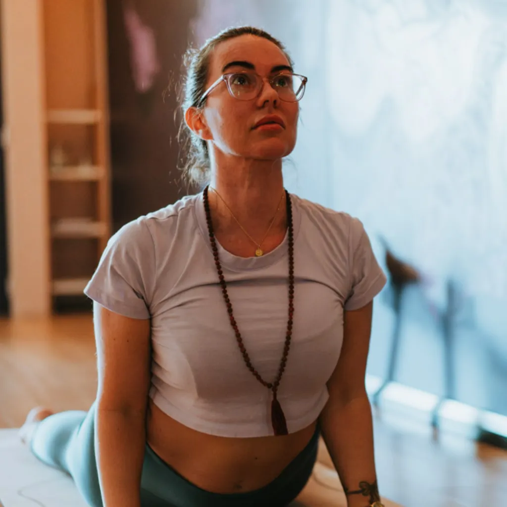 Person seated on a yoga mat with eyes closed and one hand on the belly, practising controlled breathing to regulate the nervous system under pressure.