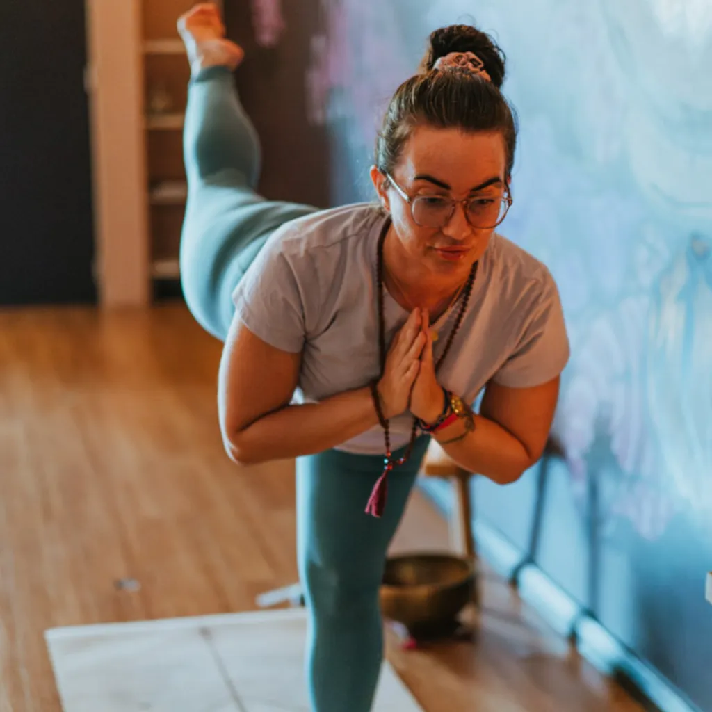 Person practising a gentle, supported deep stretch on a yoga mat in a peaceful space, eyes closed and breathing slowly, representing release and nervous system calm.
