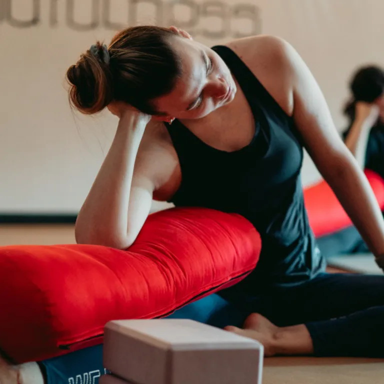 Person practicing Seated Side Bend pose on yoga mat, left arm arcing overhead while sitting cross-legged, creating a deep lateral stretch through the side body.
