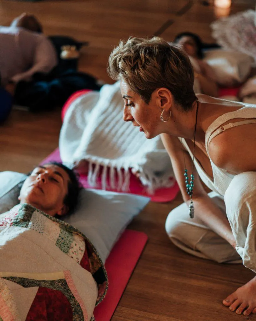 Person seated in a peaceful meditation pose on a yoga mat with one hand on the belly, practising slow breathing to support breathwork and nervous system calm.