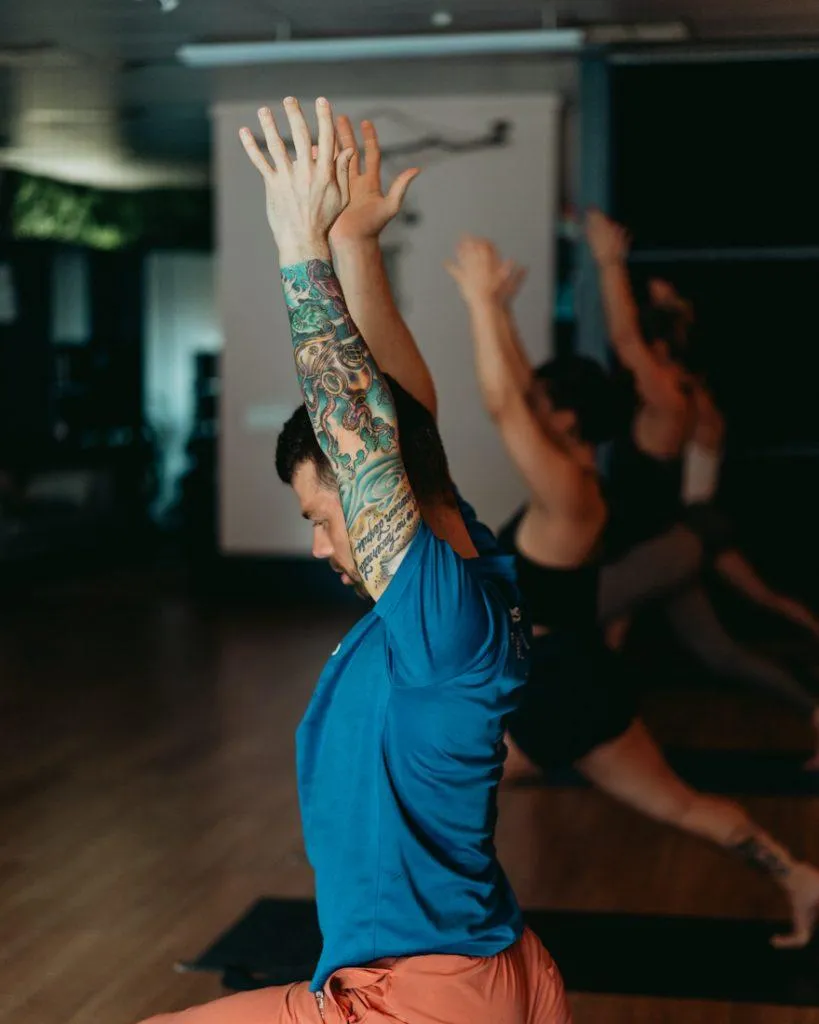 Yoga student in Low Lunge with Ankle Stretch, front knee bent deeply, back foot pointed with top of foot pressing into the mat, demonstrating ankle mobility and hip opening on a yoga mat in a well-lit studio.