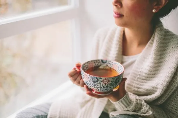 Woman in her 30s–50s with a cup of tea, in reflection. The mood: calm, elegant, introspective.