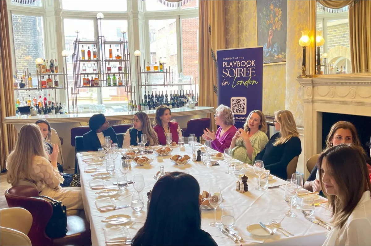 An elegant photo of a confident, diverse group of women in conversation, laughing and leaning in during a brunch or leadership circle