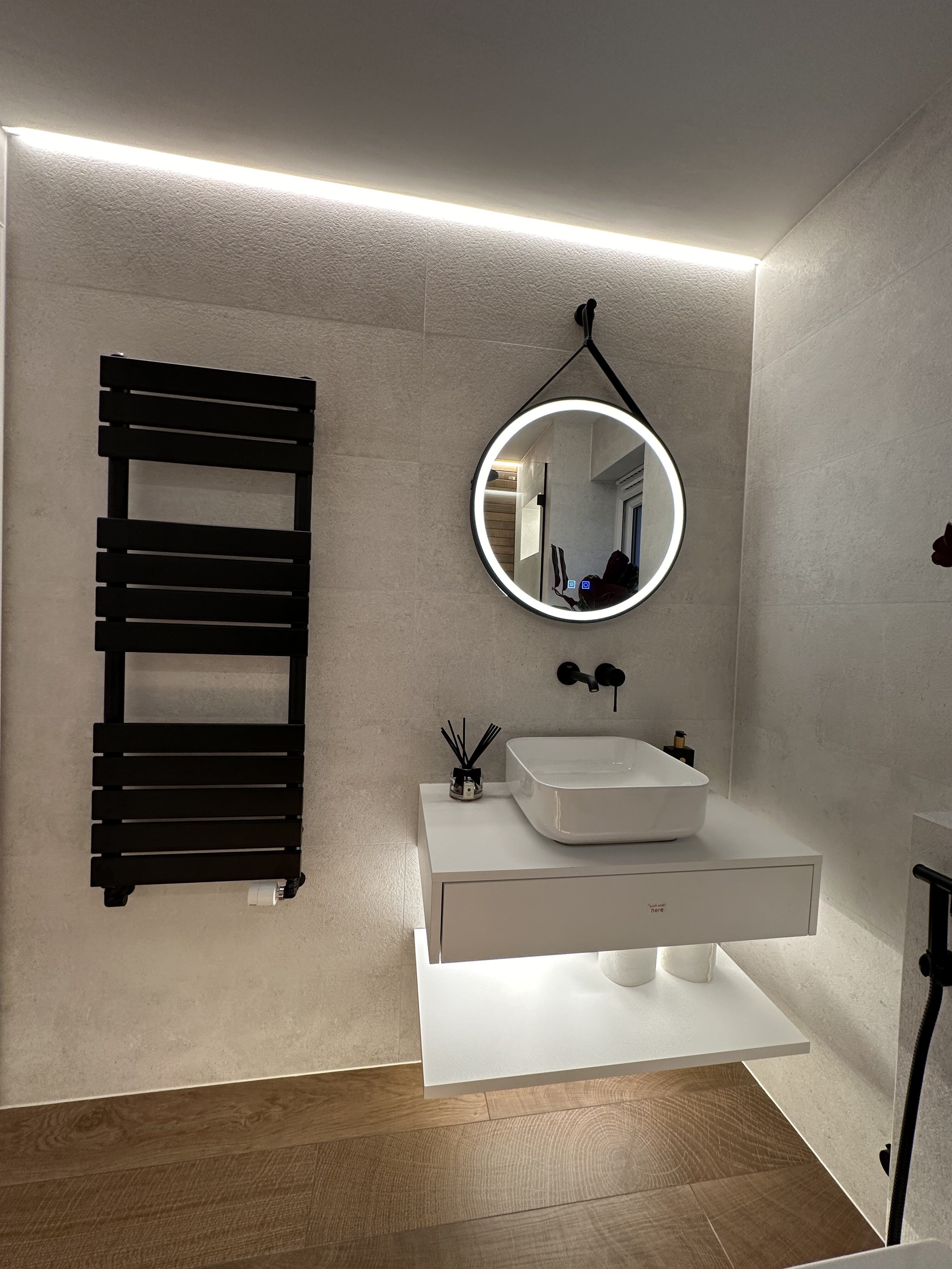 Modern bathroom upgrade in Glasgow showing a black heated towel rail, minimalist white basin, and round LED mirror, fitted and refurbished by PJTC with attention to sleek, contemporary design.