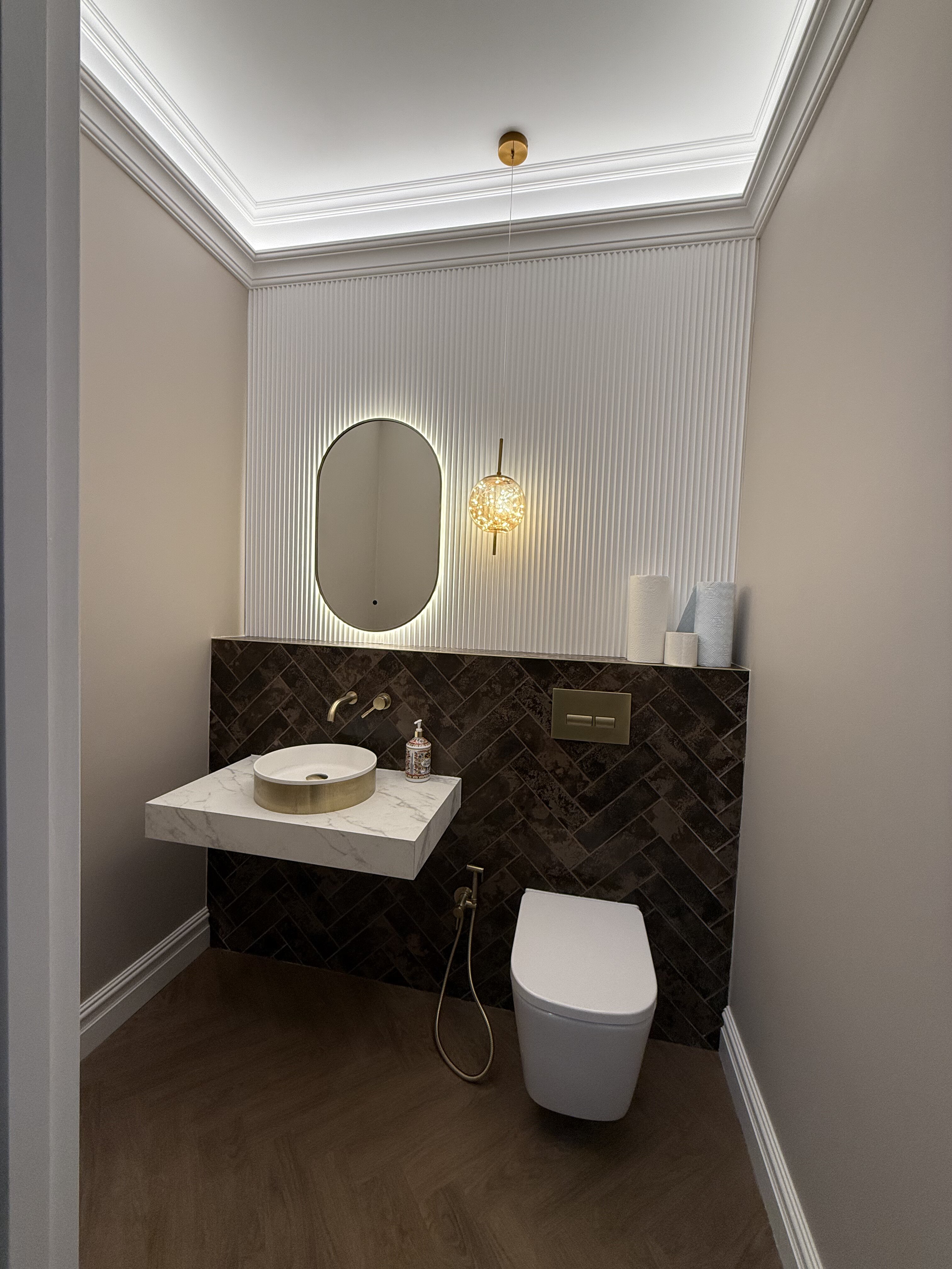 Stylish bathroom refurbishment in Glasgow showcasing a floating marble-effect vanity with round basin, illuminated mirror, and dark herringbone tiled splashback, professionally modernised and fitted by PJTC.