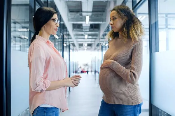 A pregnant woman looks skeptically at her co-worker as she gets baby gear advice.