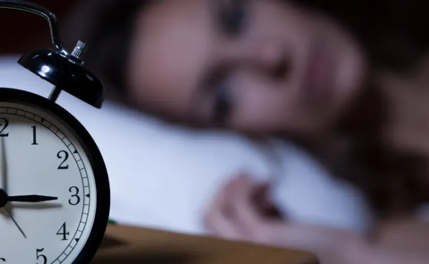 Focused on clock in foreground with blurry woman in bed behind