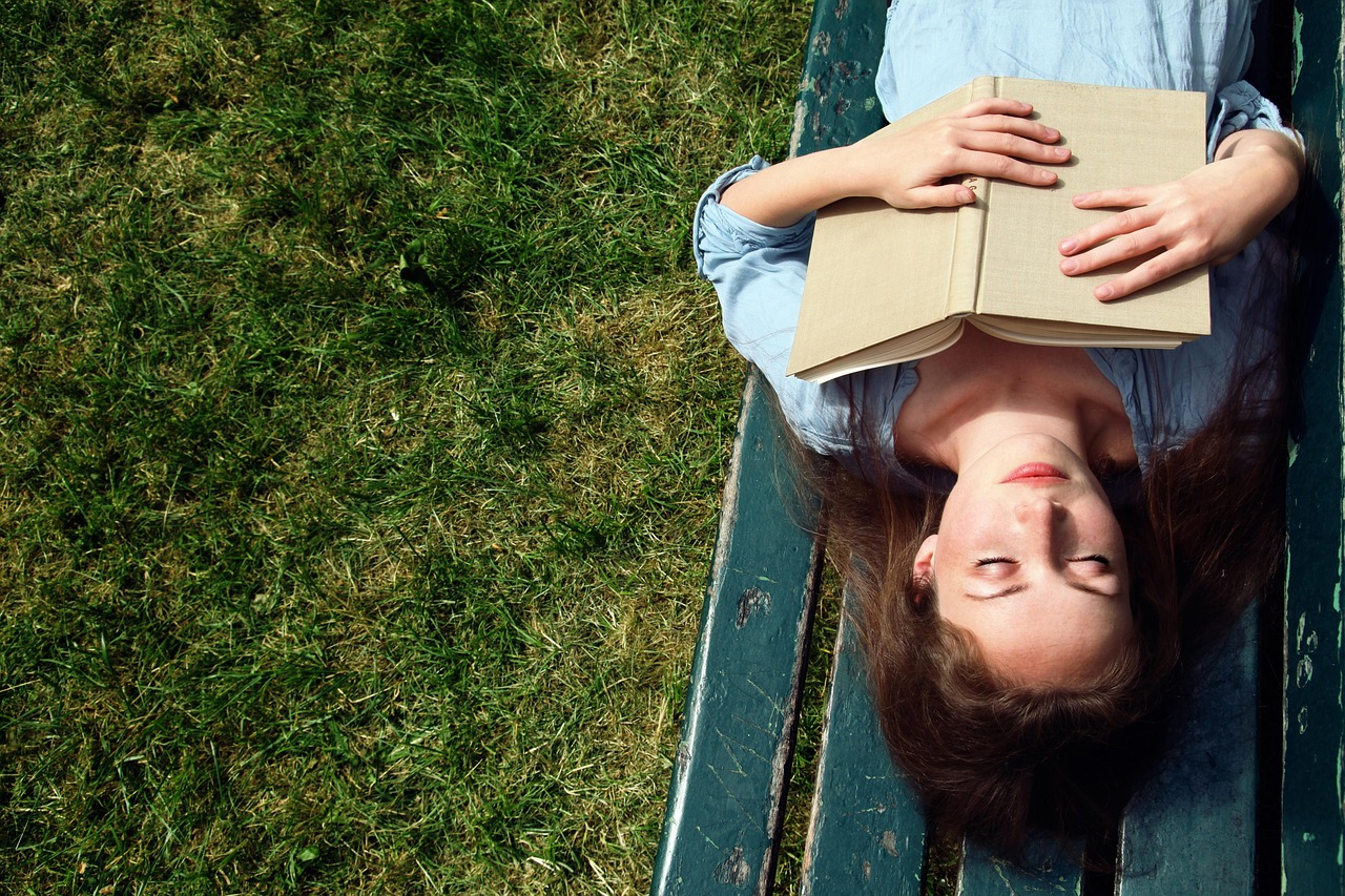 woman laying on bench eyes closed, open book on her chest