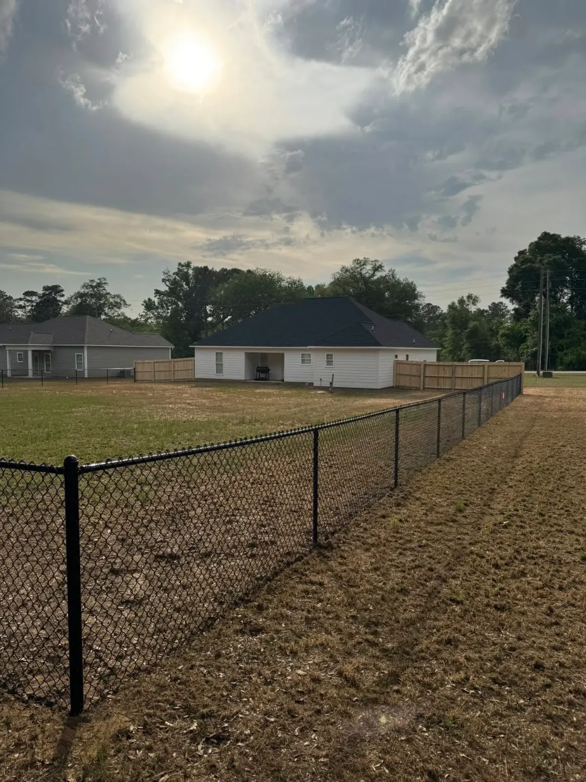 Black chain link security fence with wooden privacy fence in background, project by MCM Fence LLC, Sylvester, GA.