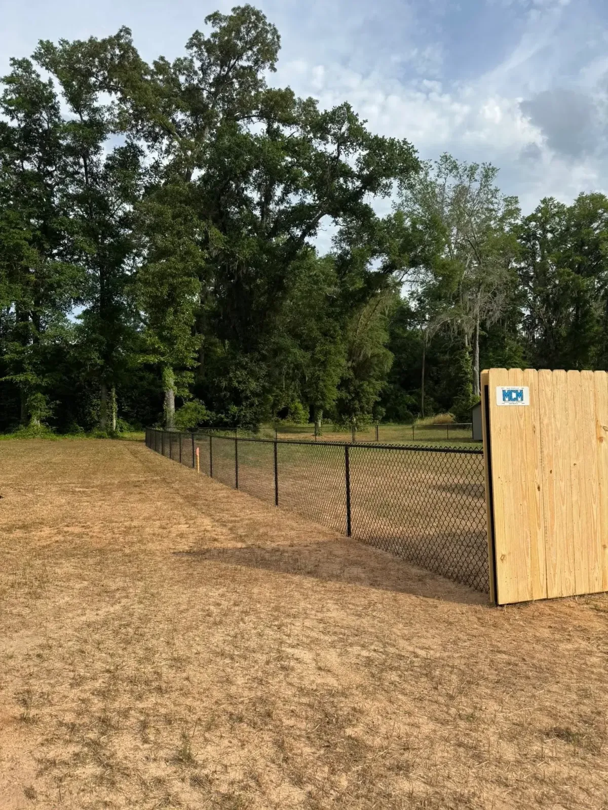 Black chain link fence with custom wooden gate section featuring MCM logo, Ashburn, GA project.