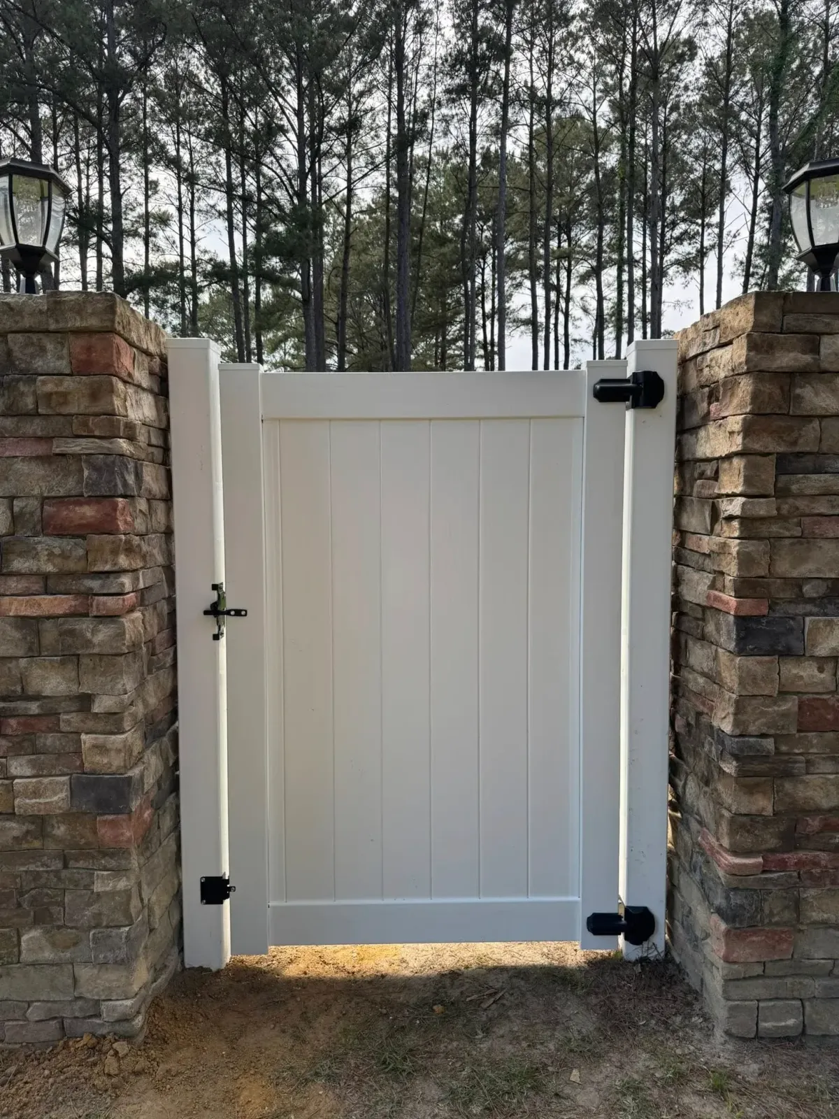 Custom white vinyl gate with black hardware and stone pillars, installed by MCM Fence LLC in Moultrie, GA.