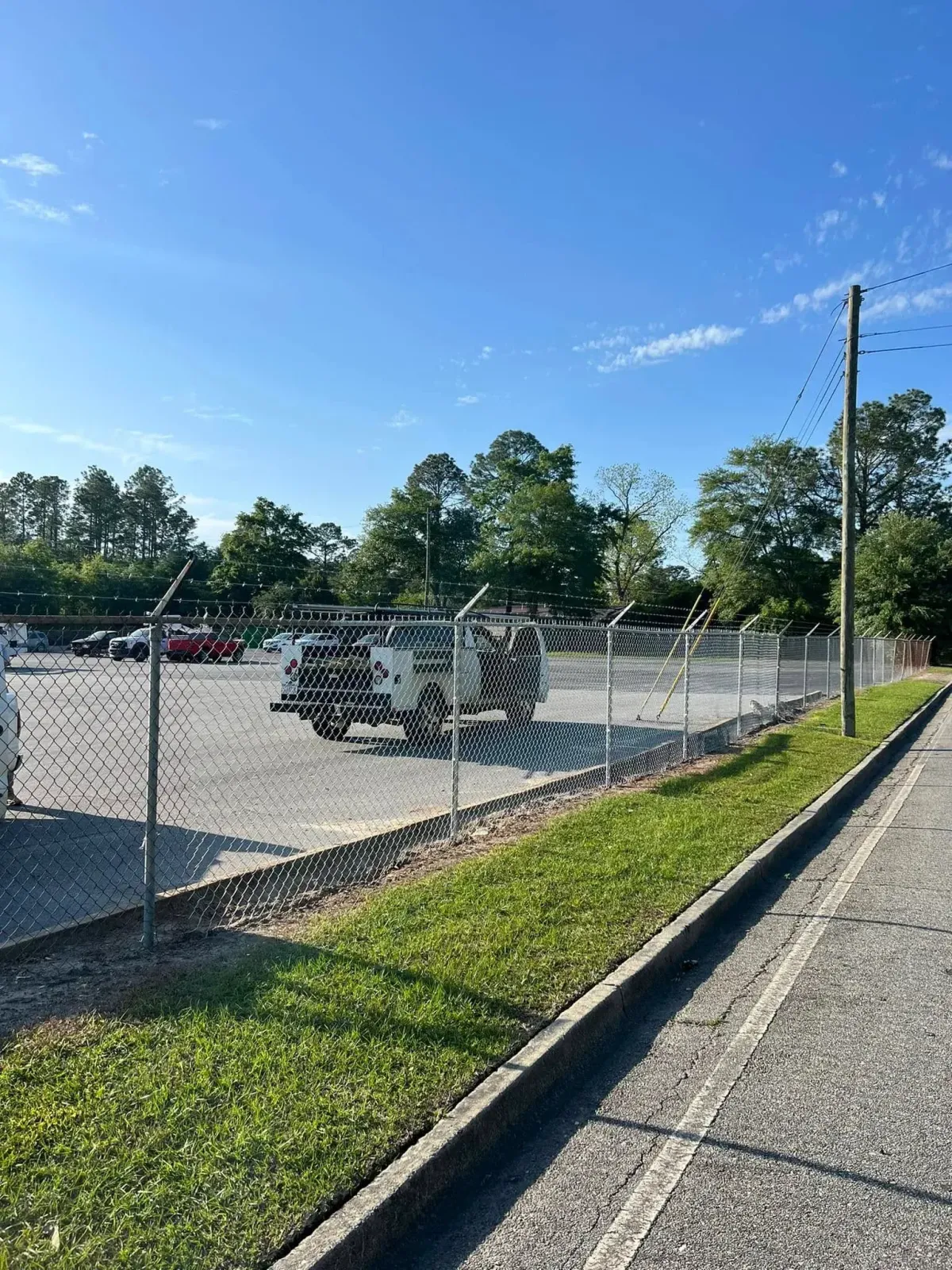 Commercial galvanized chain link fence with barbed wire security top by MCM Fence LLC in Georgia, securing a parking lot.