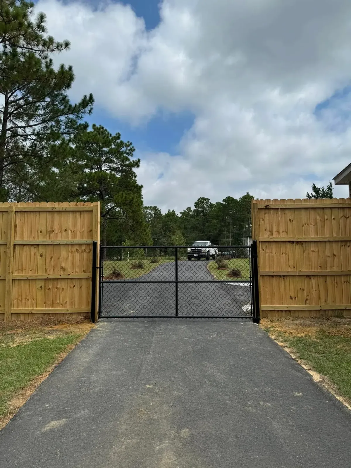 Black chain link double driveway gate set within a wooden privacy fence, a custom fencing solution by MCM Fence LLC in Georgia.