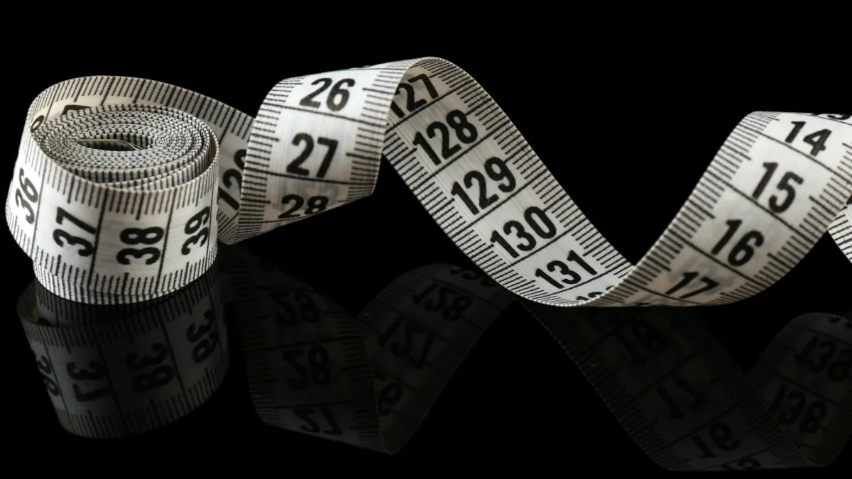 Coiled measuring tape showing inches and centimeters, symbolizing weight loss and body measurement goals, against a black reflective background.