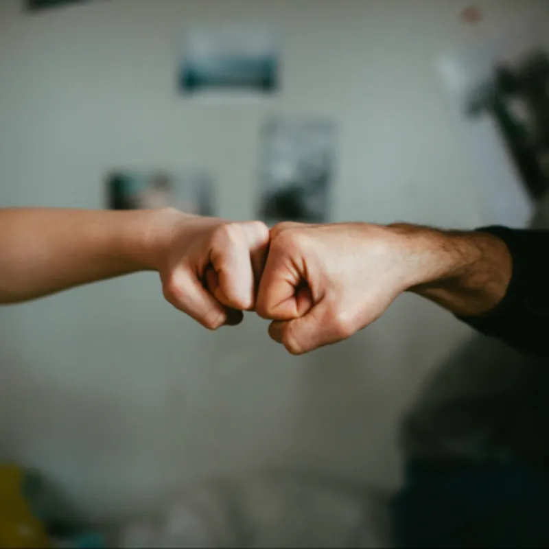 Two people performing a fist bump, symbolizing support, encouragement, and partnership. The background is softly blurred, drawing focus to the gesture of connection.