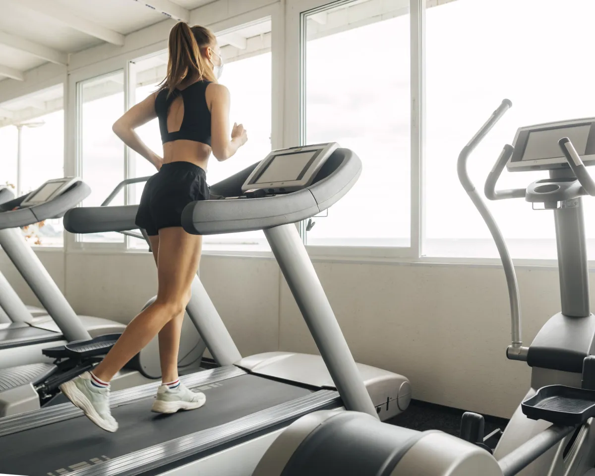 Young woman running on a treadmill in a bright gym, representing moderate exercise during later phases of the Hyper-Ketosis program