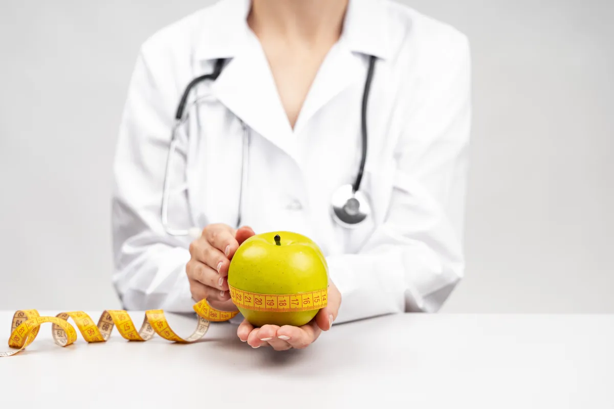 Healthcare professional holding a green apple wrapped with a measuring tape, symbolizing medical support for weight management and metabolic health.