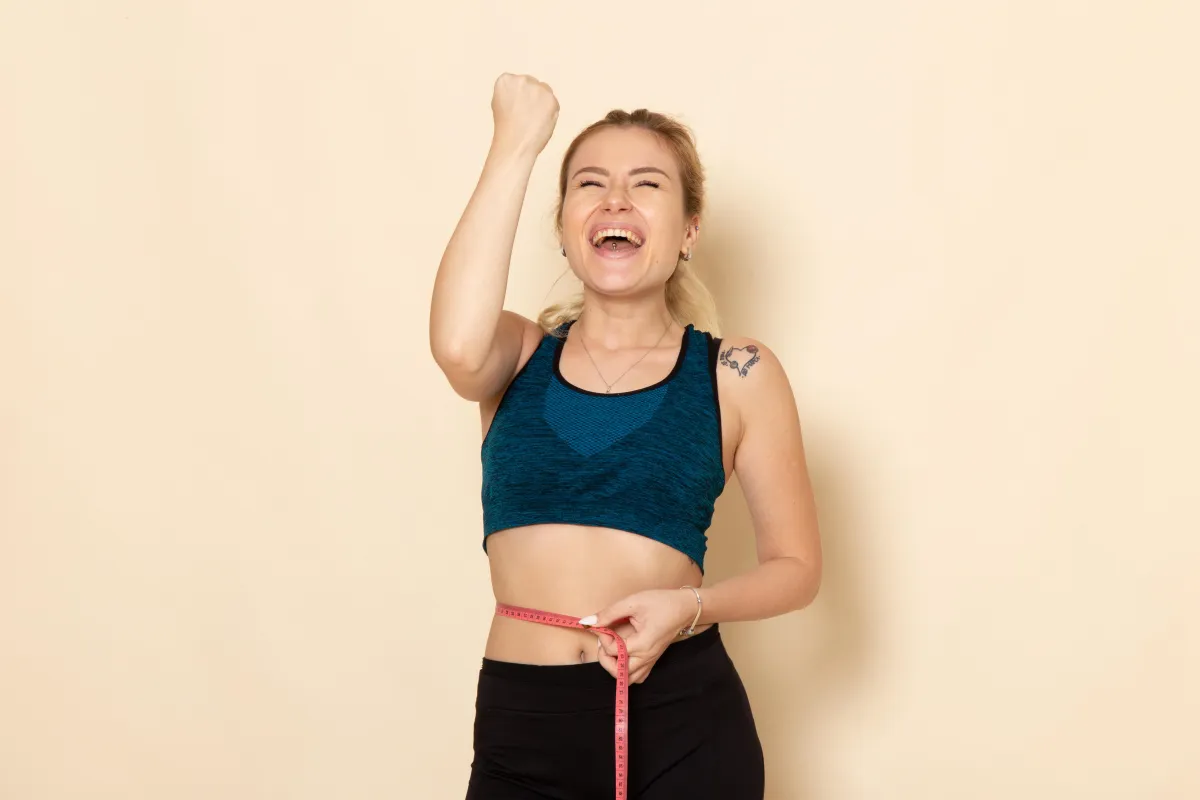 Young woman in athletic wear measuring her waist with a tape measure, symbolizing transformation, accountability, and progress—perfectly aligned with the goals of the Hyper-Ketosis Rapid Weight Loss Challenge.