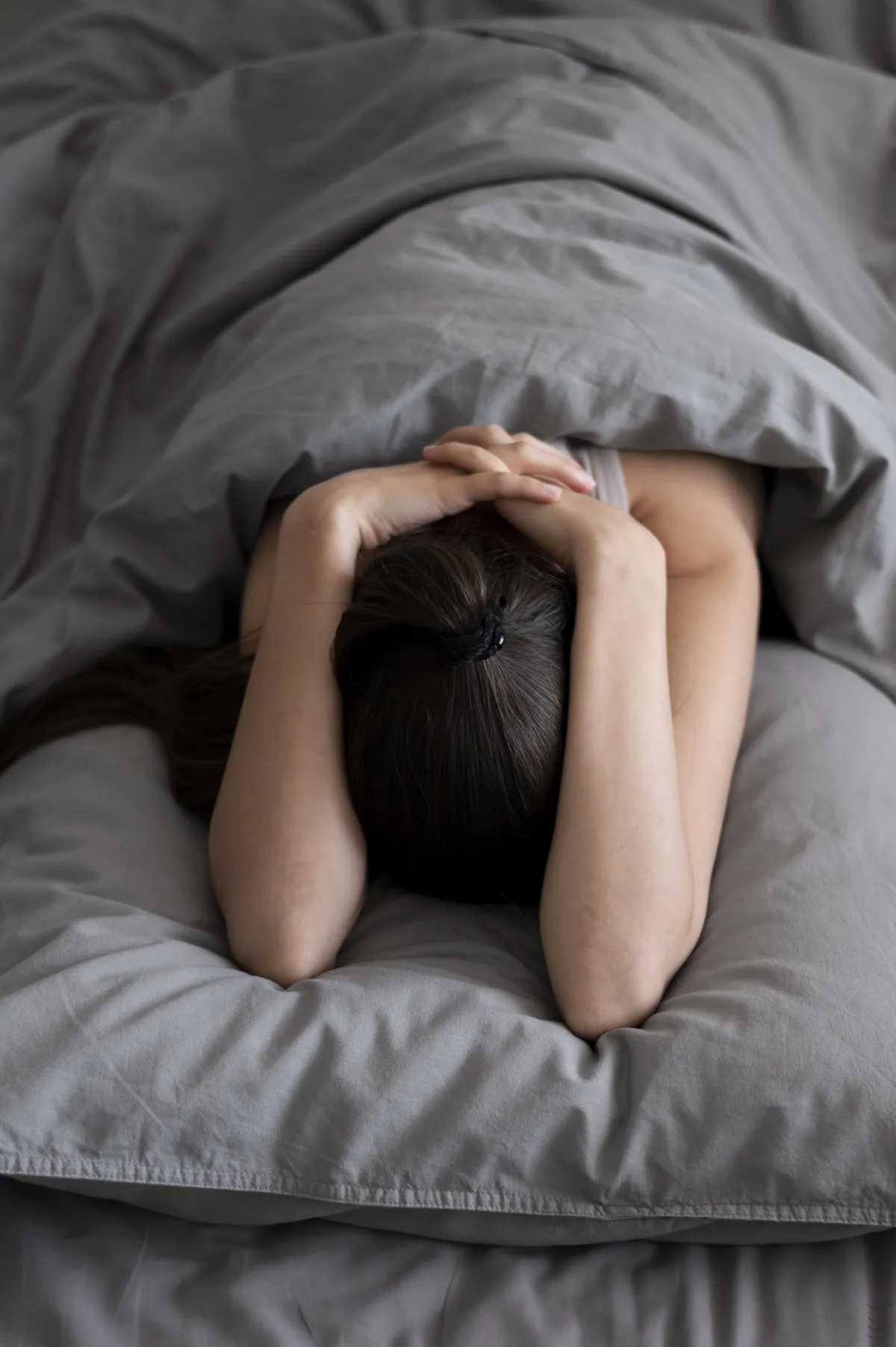 Tired woman sitting on bed with head in hand, symbolizing how stress and poor sleep can stall fat loss on Hyper-Ketosis.