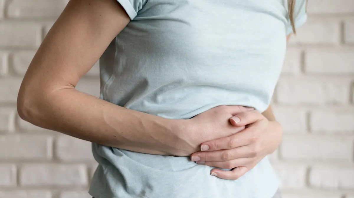 Woman holding her stomach, experiencing bloating or digestive discomfort — a common symptom improved by the Hyper-Ketosis gut healing approach.