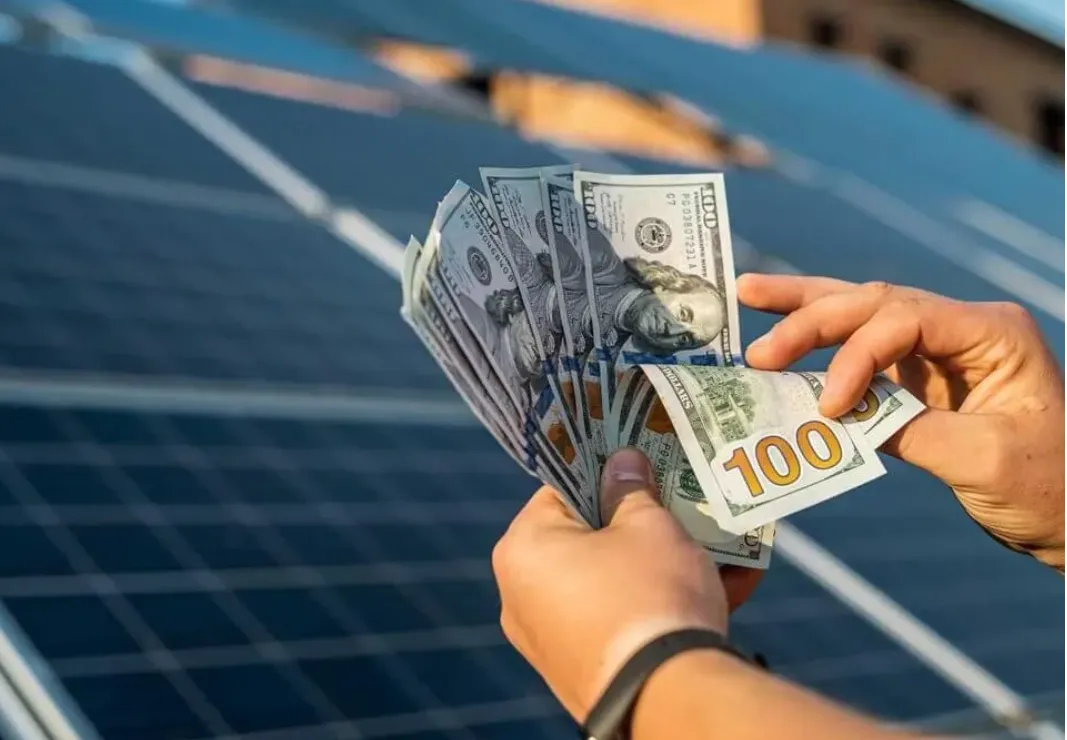 hands counting money in front of solar panels