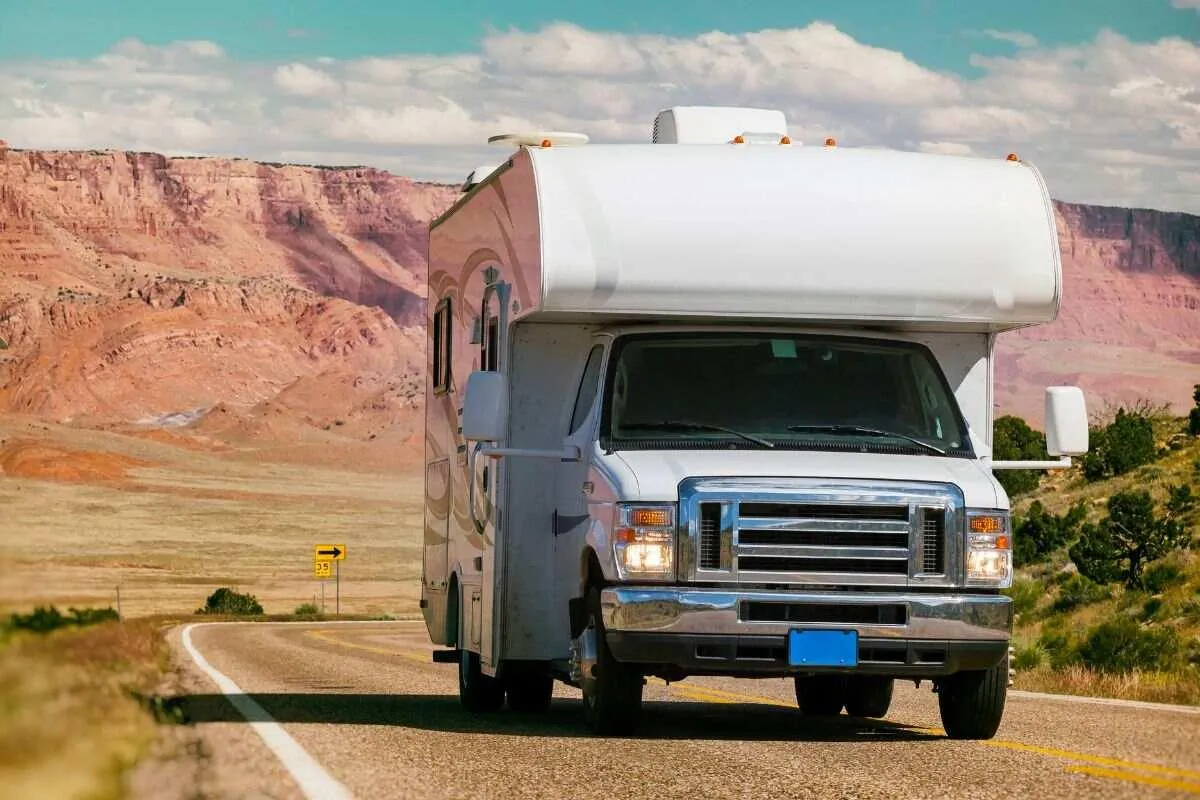An RV driving on a Montana road with scenic mountains and a clear sky in the background