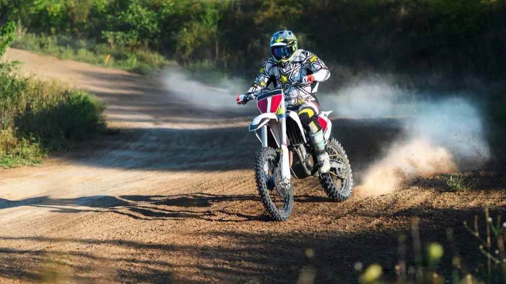 A dirt bike rider in protective gear rides through dirt, showcasing the need to make a dirt bike street legal for road use.