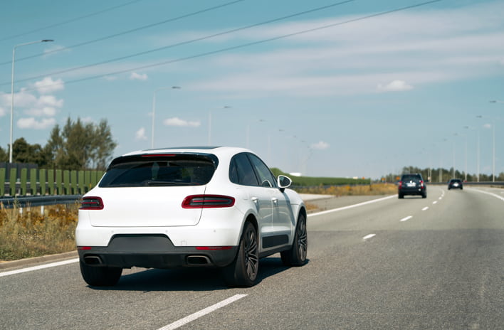 White Porsche Macan driving on a North Carolina highway, symbolizing the process of transferring a car title in North Carolina.