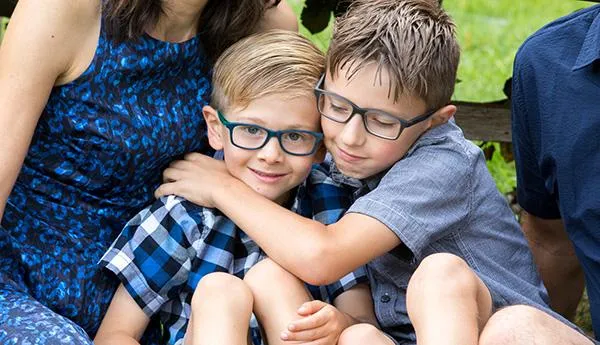 A picture of four siblings laying on each other in different positions, smiling at the camera, and there's a white picket fence as a backdrop.