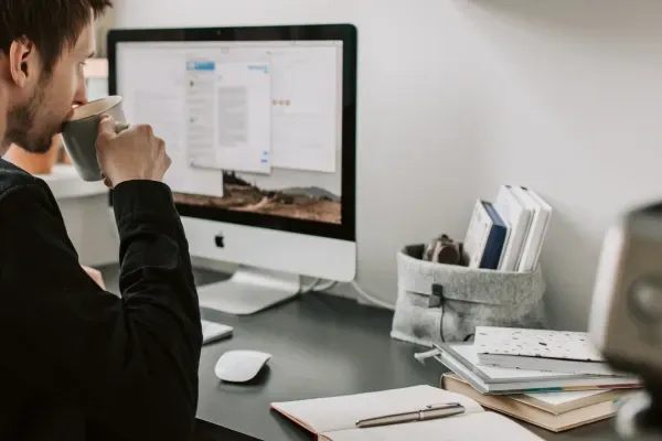 Toimistotyöntekijä juomassa kahvia näytön äärellä