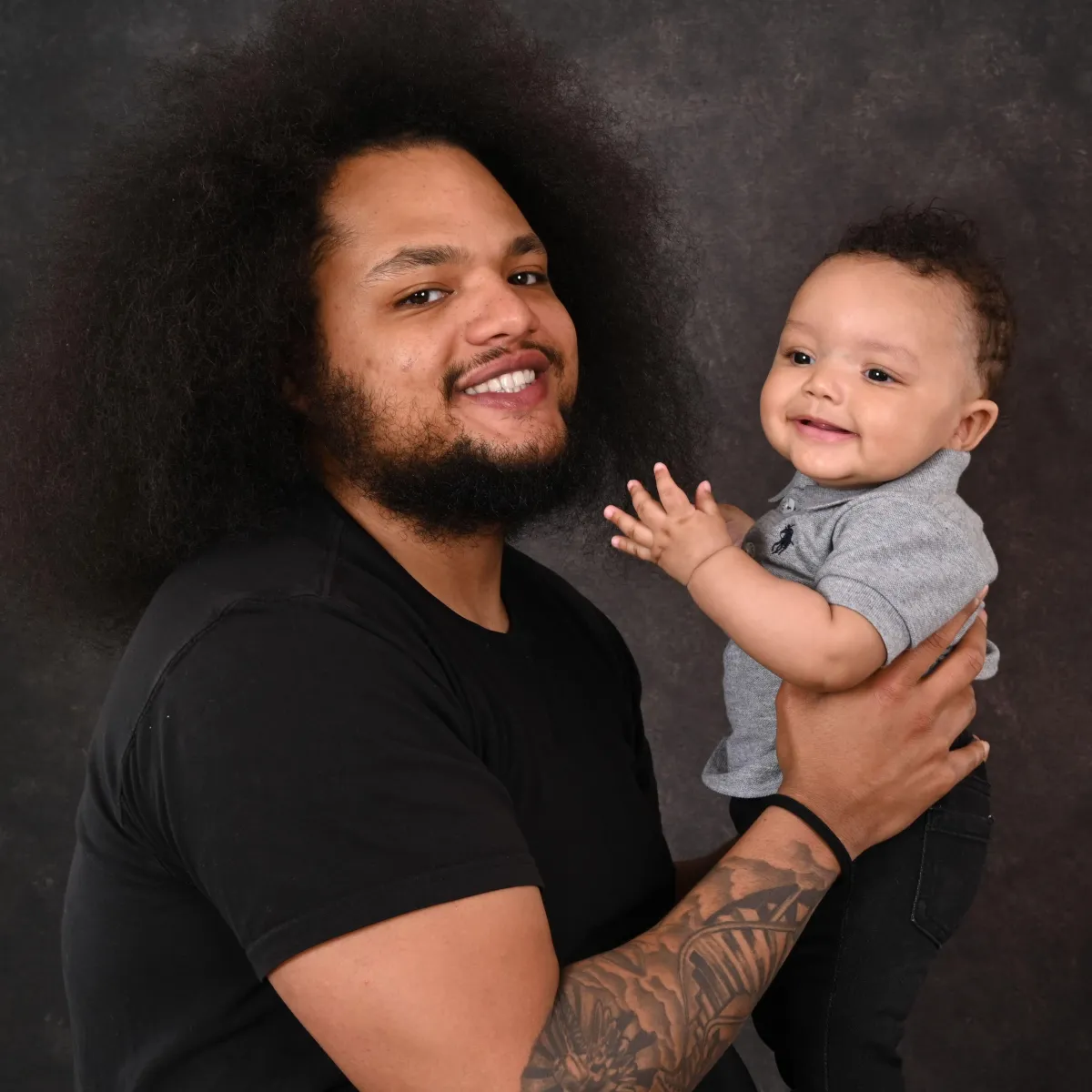 Dad and son smiling together in a photo. Dad is carrying is son with pride and joy.