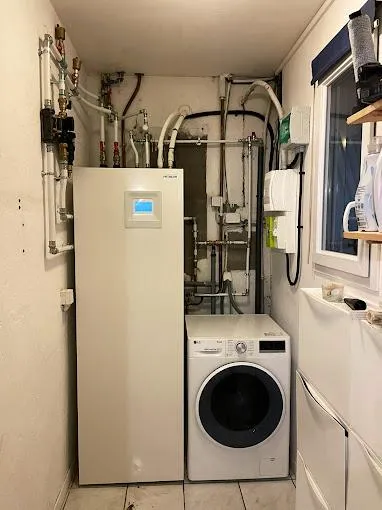 Ballon thermodynamique blanc installé dans une petite buanderie, raccordements hydrauliques et électriques par AFO Énergies à Lapeyrouse-Fossat.