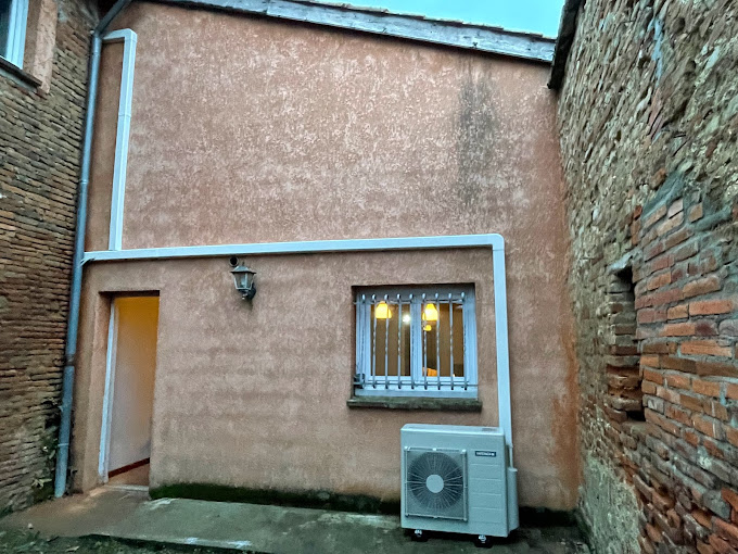 Unité extérieure de climatisation installée dans une cour de maison en pierre ocre à L'Union, avec goulotte blanche verticale, par AFO Énergies.