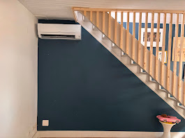 Climatiseur mural installé sous un escalier en bois dans un salon au mur bleu foncé par AFO Énergies à Toulouse, pour assurer une climatisation réversible discrète.