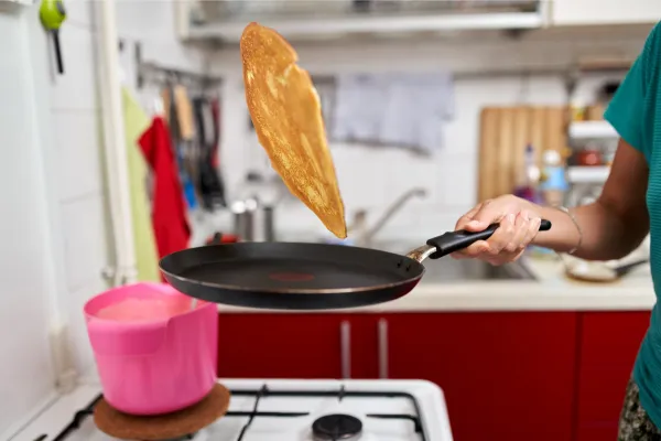 A person flipping a golden pancake in a frying pan in a kitchen with red cabinets, symbolizing how Cash Clarity helps business owners 'flip' their approach to financial management with our 'Small Plates' system inspired by Profit First principles