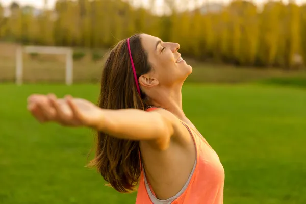 A woman with her arms stretched wide, her eyes closed, and smiling while soaking in the outdoors.