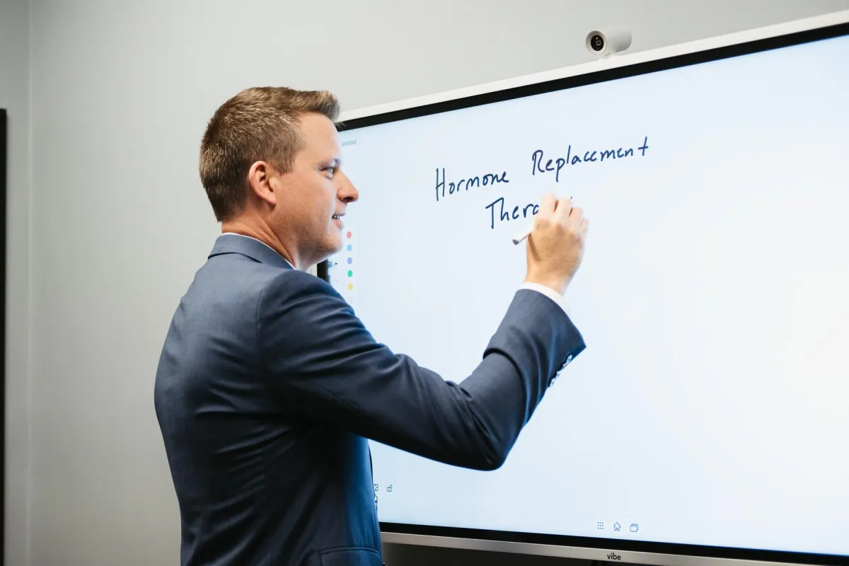 Dr. Ambrose writing "Hormone Replacement Therapy" on a Vibe board.