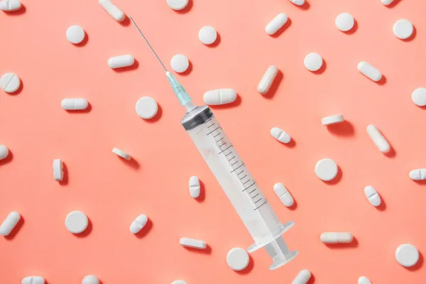 A syringe on top of a background of pills. 