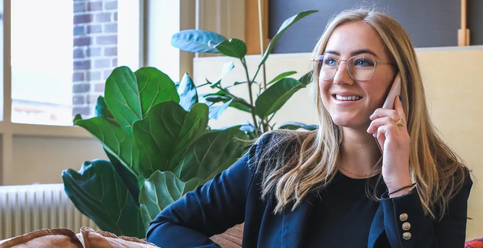 En blond affärskvinna med glasögon sitter i en soffa och pratar i telefon