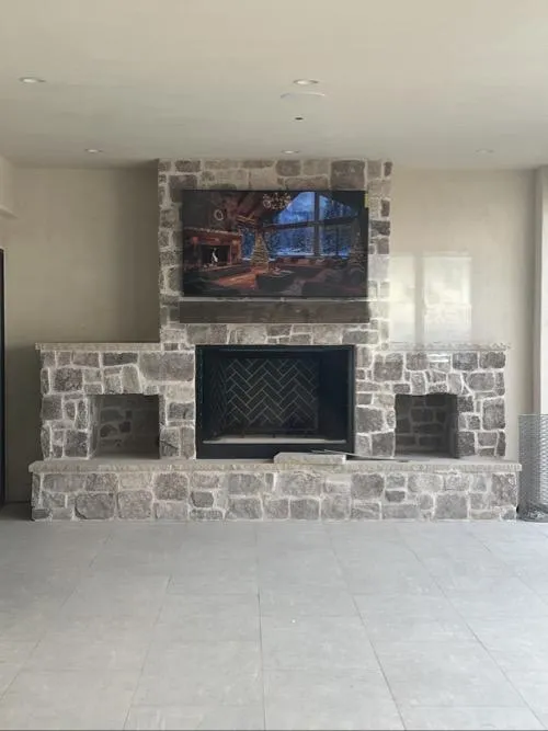 Stone fireplace with built-in shelving and mounted TV displaying a cozy cabin scene.