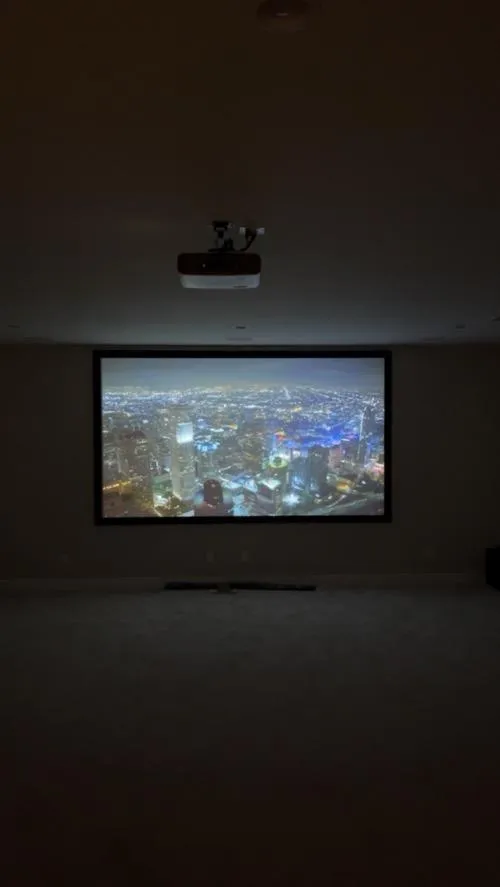 Home theater with ceiling-mounted projector displaying a cityscape on a large wall screen in a dark room.