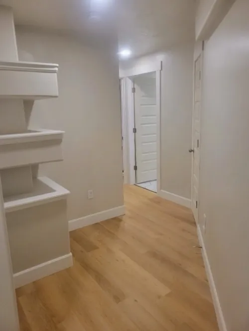 Basement hallway remodel with wood flooring and built-in shelves.