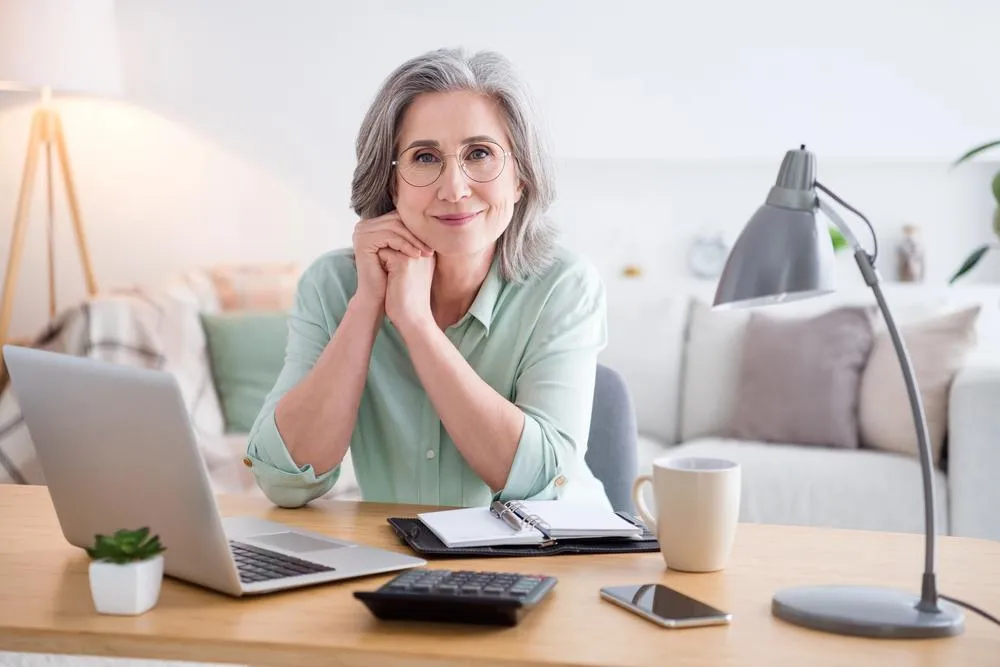 Photo of candid attractive lady sit behind desk hand on cheek look camera have good mood working from home indoors