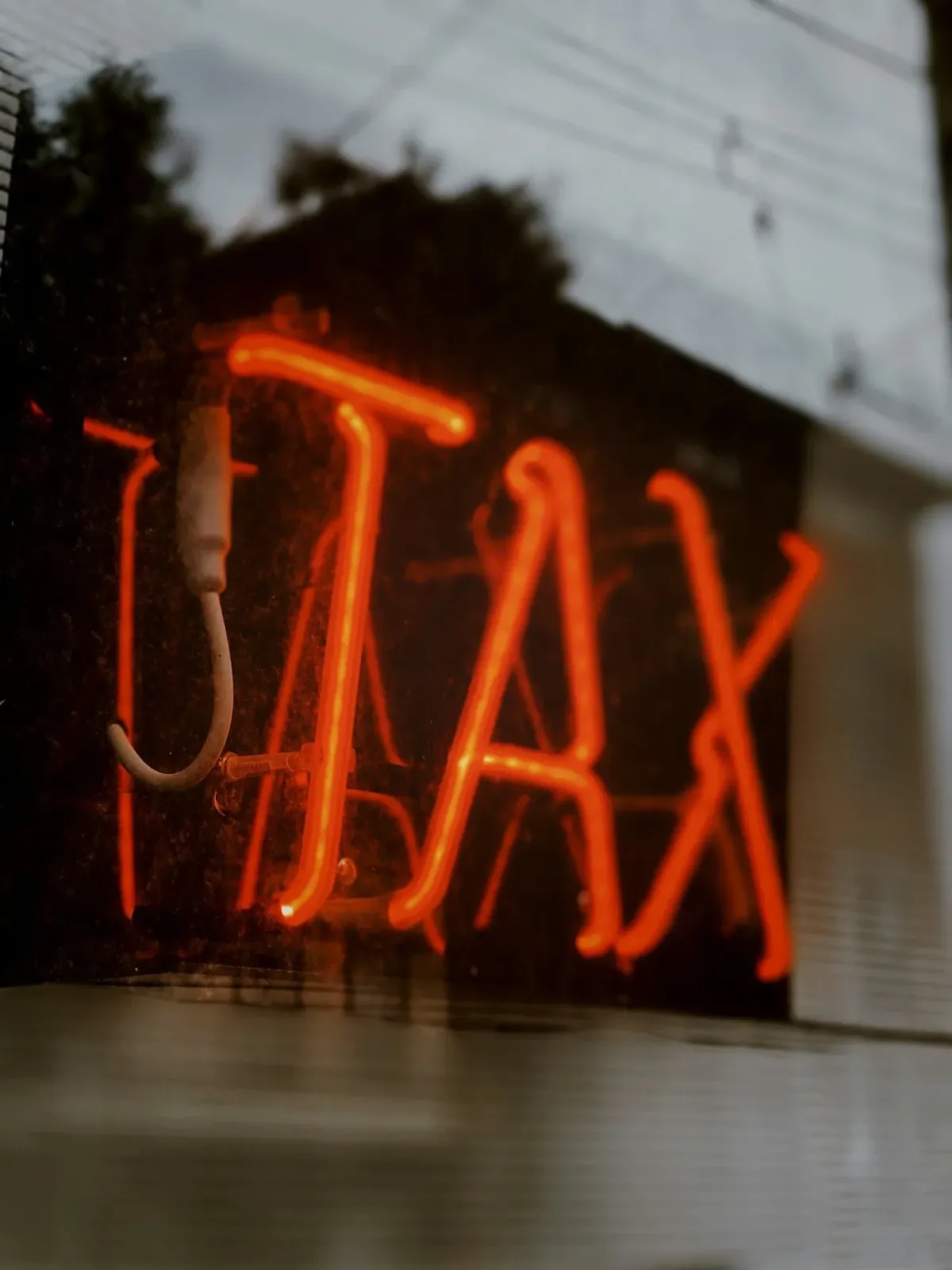 Neon red sign displaying the word “TAX,” symbolizing the hidden financial, time, and emotional costs known as the ADHD Tax.