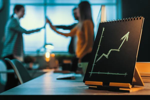 Two business people talking in an office, with a rising growth chart on a desk in the foreground