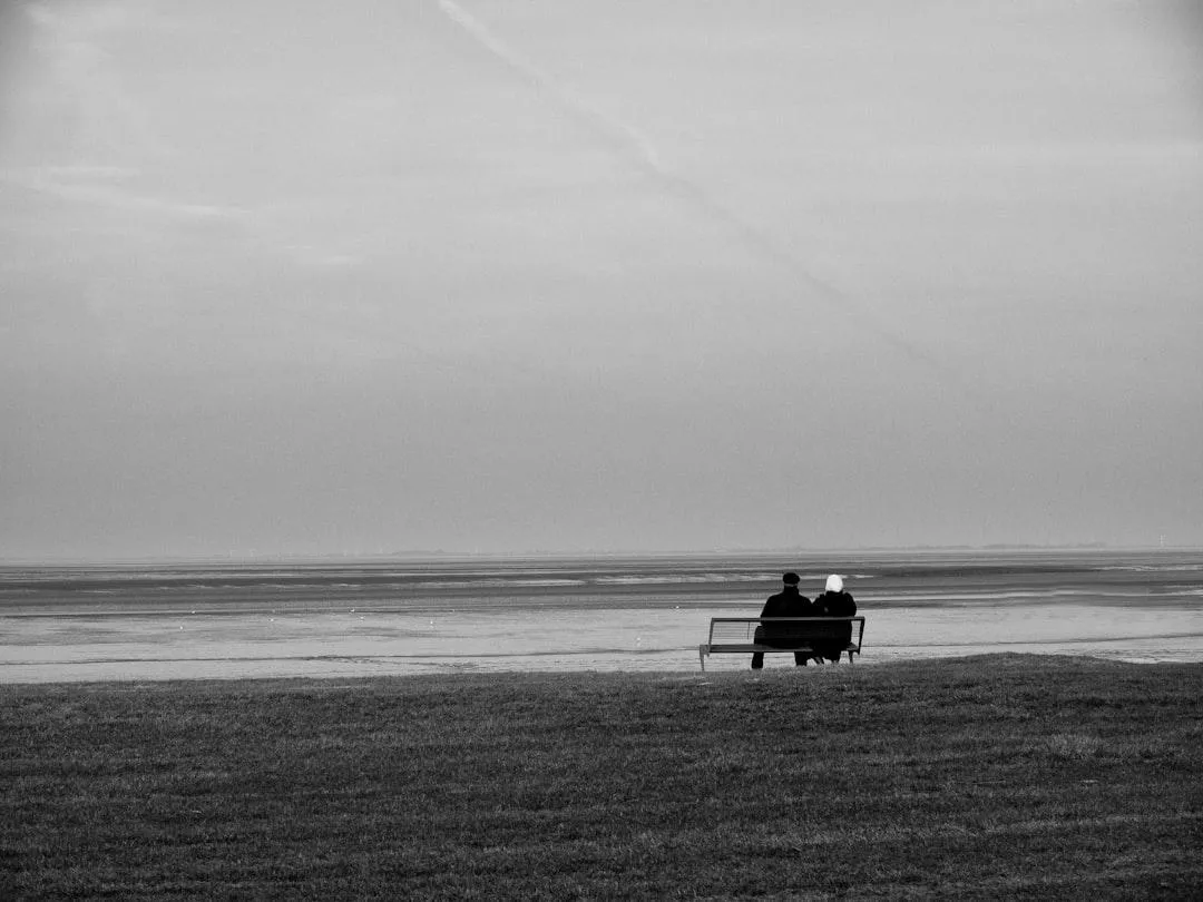 couple on beach sitting on bench in black and white
