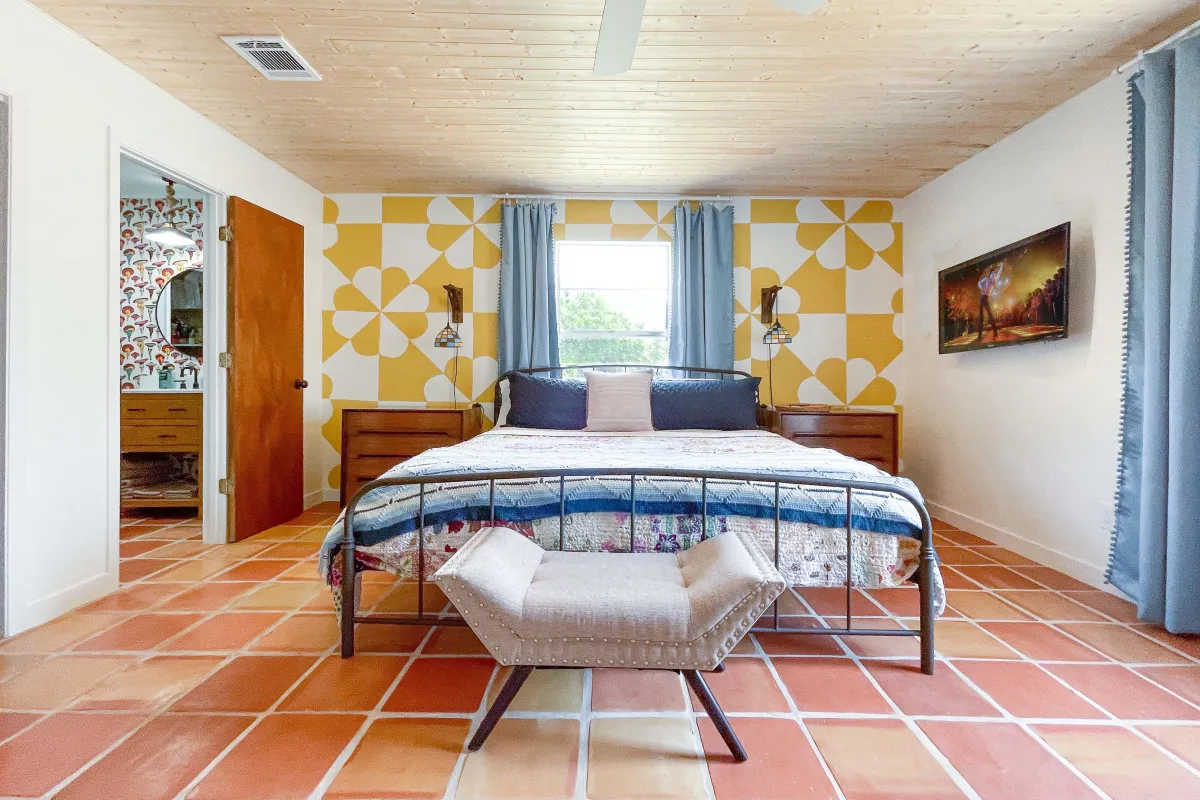 A well designed 1970s inspired vaction rental bedroom with a mural and saltillo tile