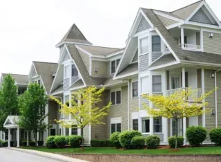 Tan apartments with beautiful trees in front.